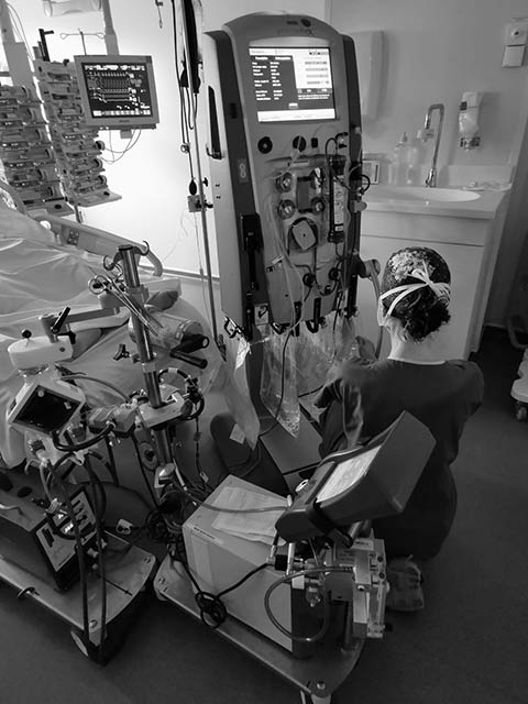 Un chirurgien en tenue stérile verte opère un patient allongé sur une table d'opération recouverte de champs chirurgicaux bleus dans un bloc opératoire équipé de divers appareils médicaux.
